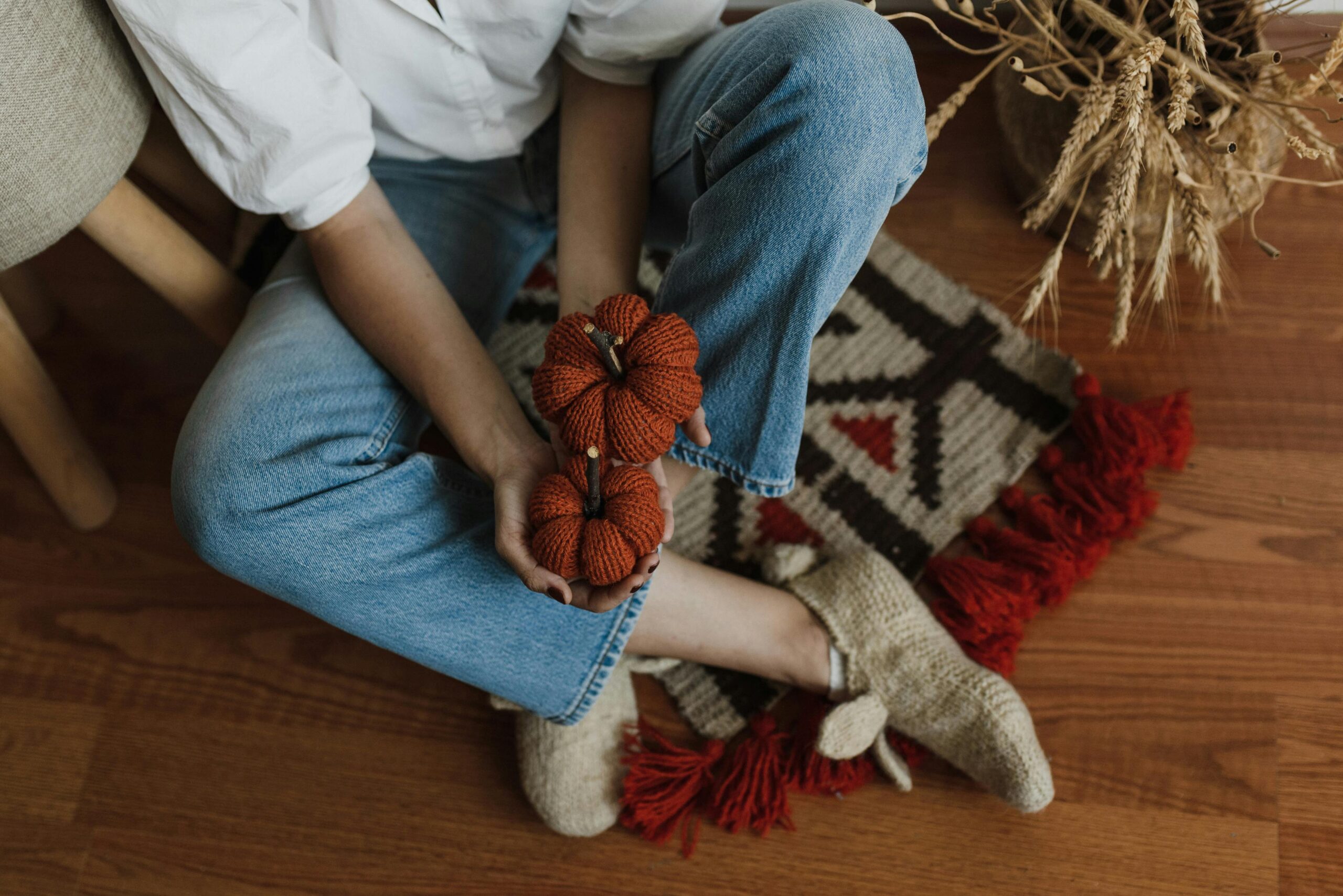 Woman Sitting on the Floor at Home Holding Red Knitted Pumpkins in Hands