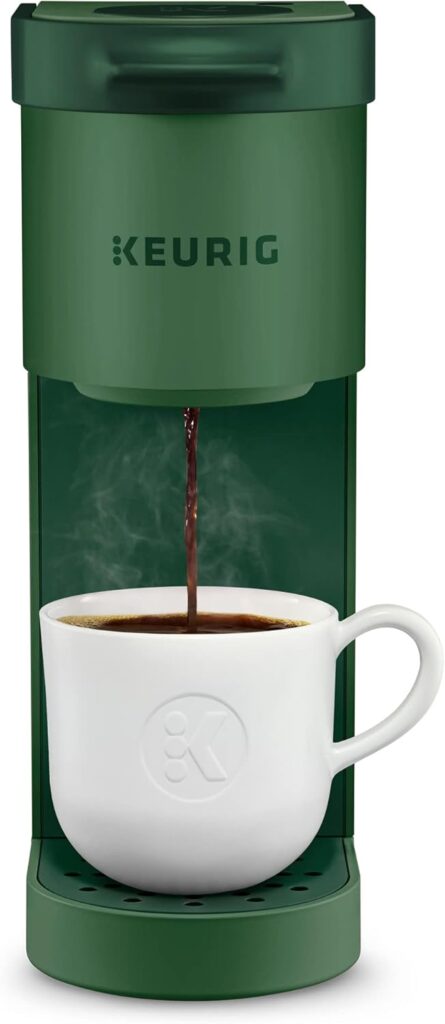 A green Keurig coffee maker brewing coffee into a white cup, with steam rising from the freshly brewed beverage.