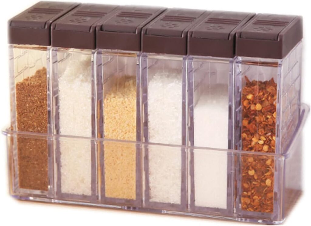A clear spice organizer with six compartments holding various spices like salt, sugar, and chili flakes.