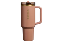 A pink Stanley travel mug with a handle and a gold accent on the lid.
