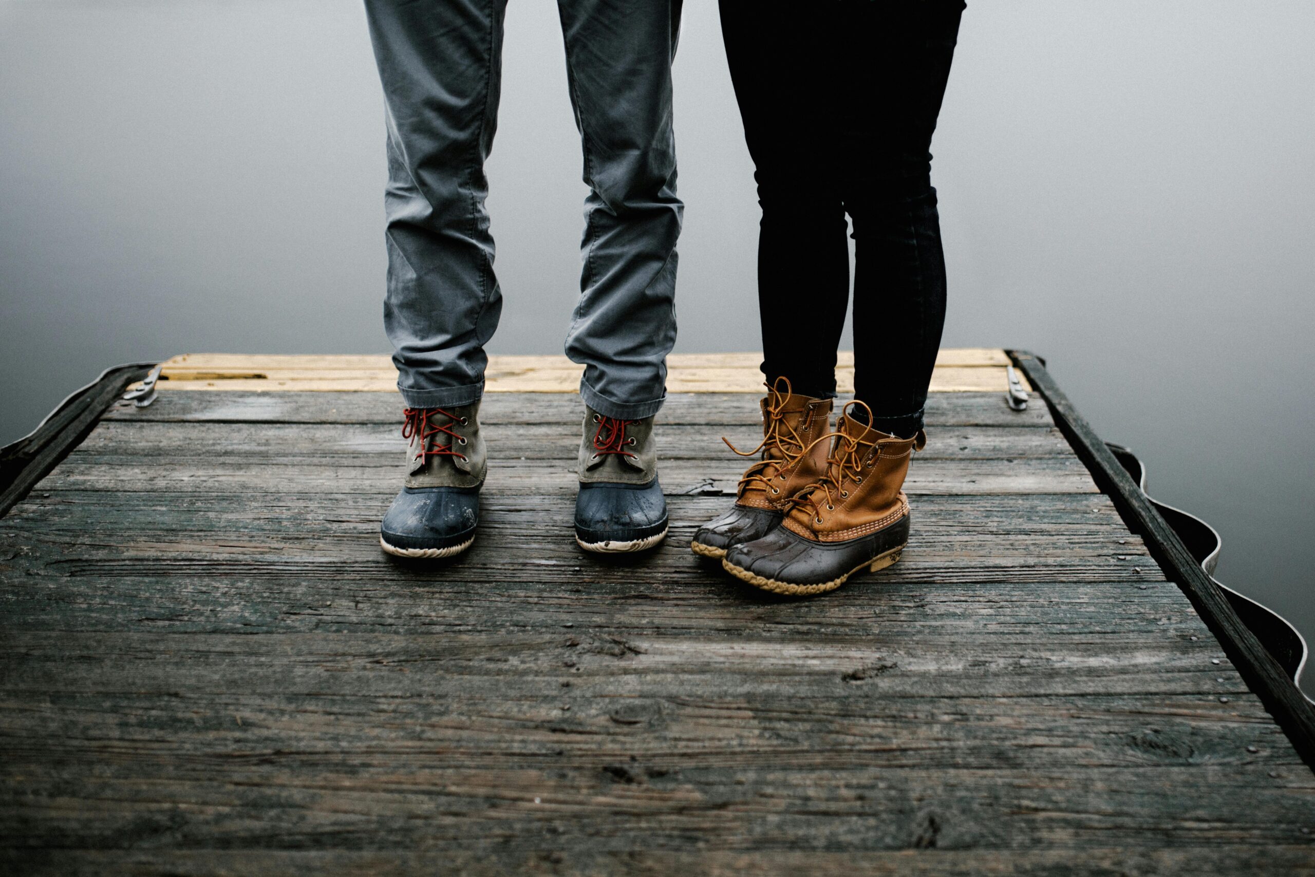 two people wearing Sperry Salt Water Duck Shoes on a dock near a lake.
