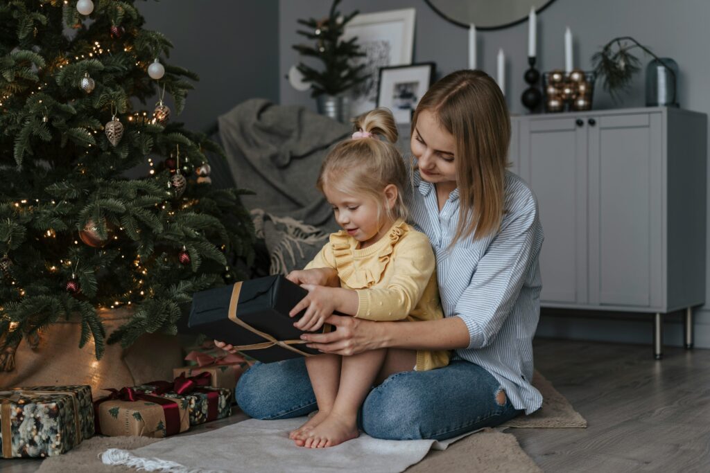 Toddler and Mom opening up screen-free Christmas gift under Christmas tree in living room.