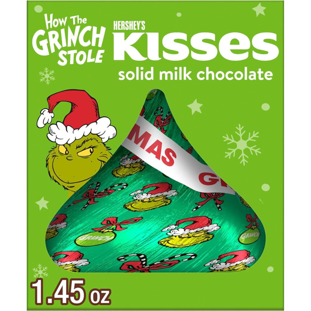 The animated Grinch pokes his head from behind a giant, wrapped Hershey Kiss chocolate