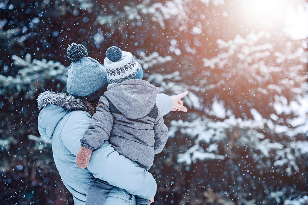 A mother holds her child and points at a snow-covered pine tree