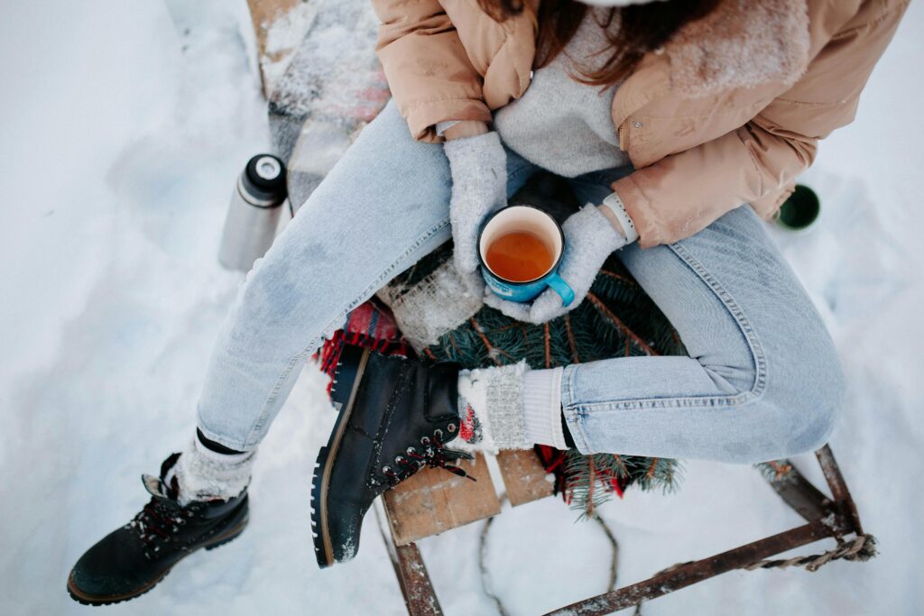 Woman sitting on sled with a cup of tea in the winter snow.