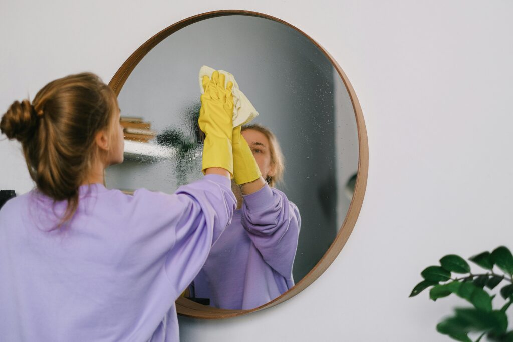 Woman in light purple sweatshirt spring cleaning her mirror.