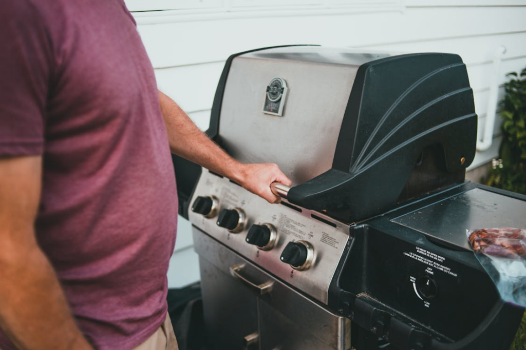 Person grilling outdoors on a stainless steel gas grill, perfect for Memorial Day BBQ deals and backyard cookout essentials.