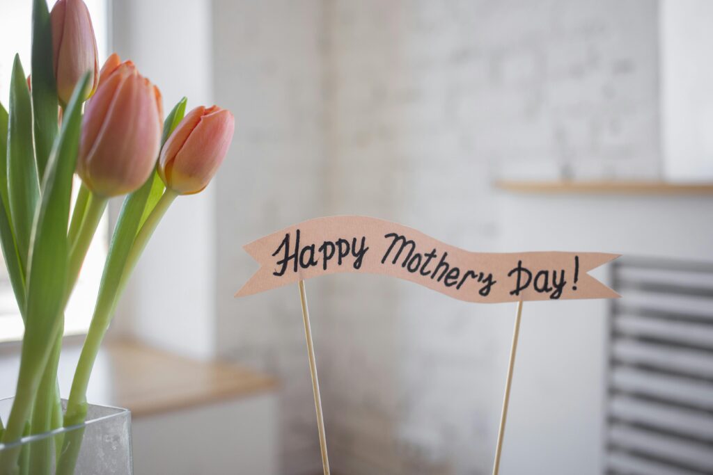 Happy Mother's day banner next to peach color tulips in a vase.