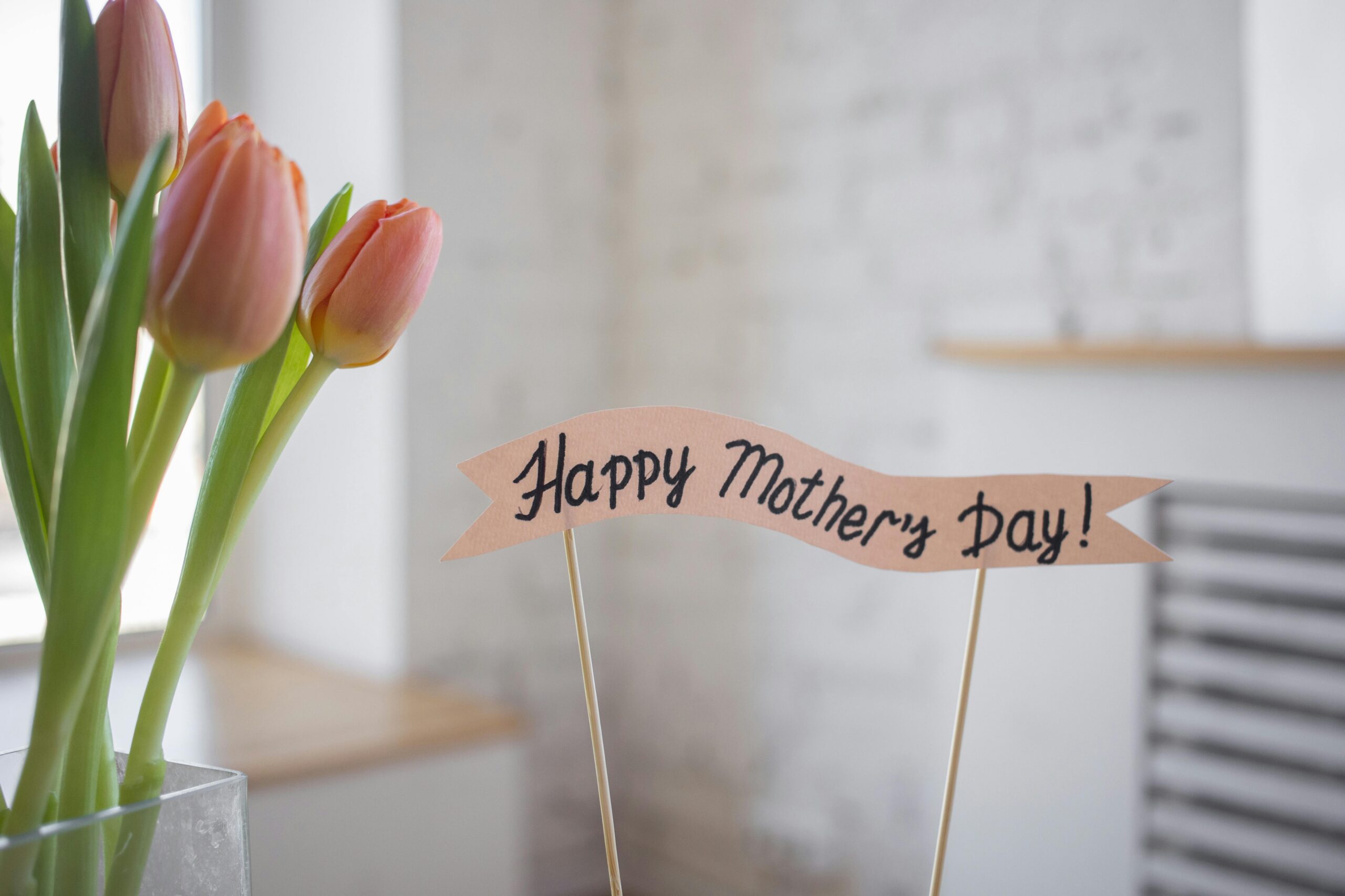 Happy Mother's day banner next to peach color tulips in a vase.