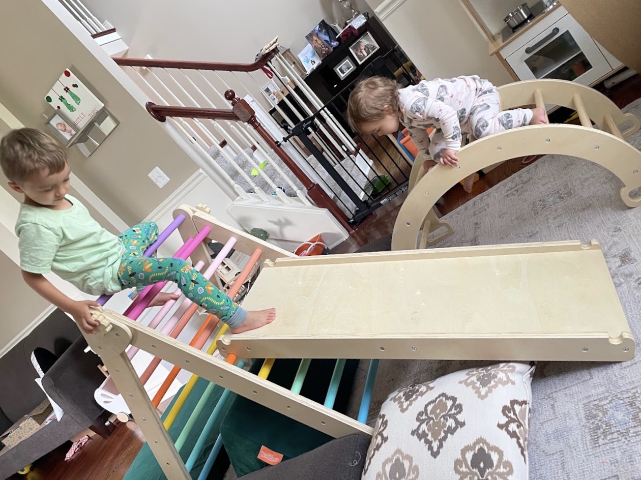 Two kids climbing a Pikler triangle with ramp and a wooden arch rocker in our living room