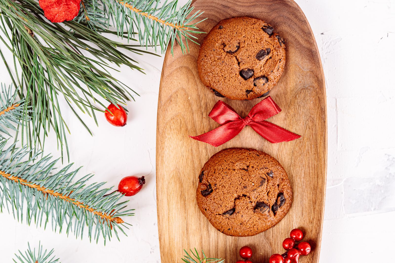 Easy Christmas cookies: chocolate chip cookies on a wooden plate with pine branches and a red bow