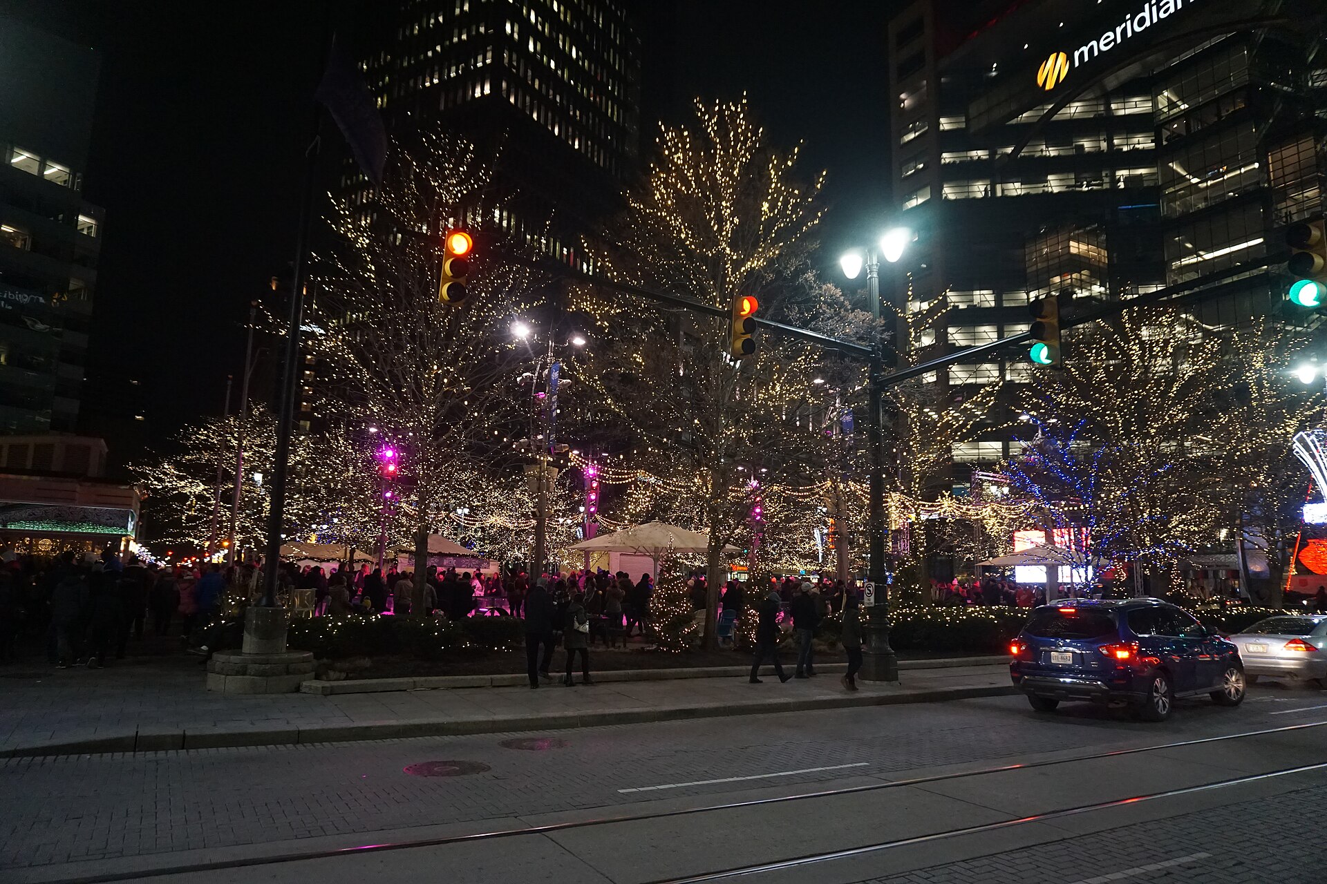 Woodward Avenue in downtown Detroit at night, lined with holiday lights and crowds near Cadillac Square