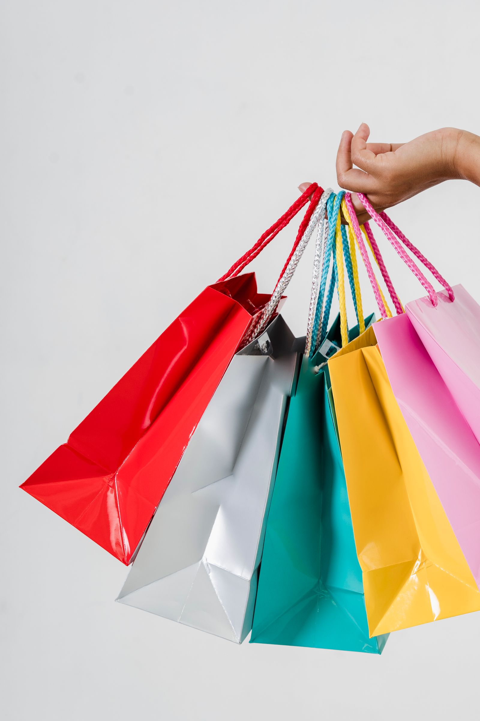 A hand holding several colorful paper shopping bags