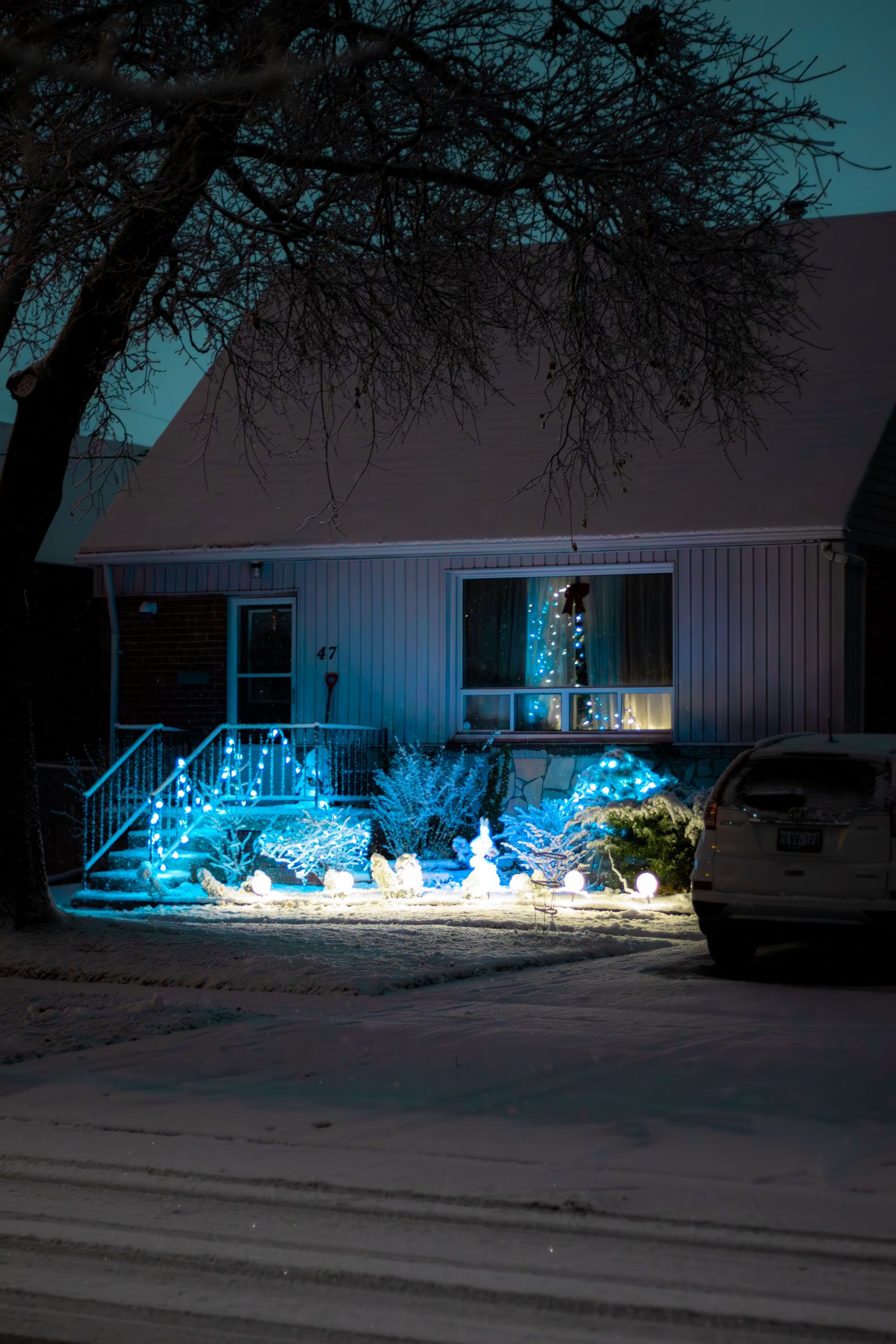 A house lit with blue Christmas lights on a snowy street