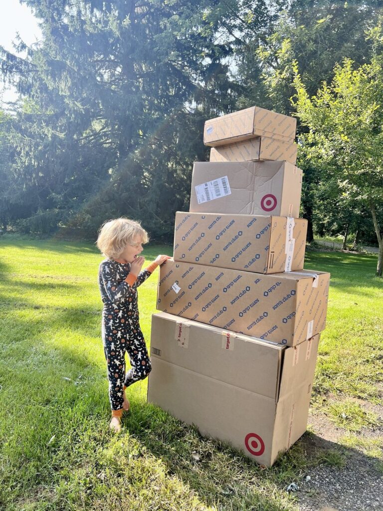 Toddler in Halloween pajamas next to a tower of Sam's Club and Target delivery boxes before Sam's Club Black Friday