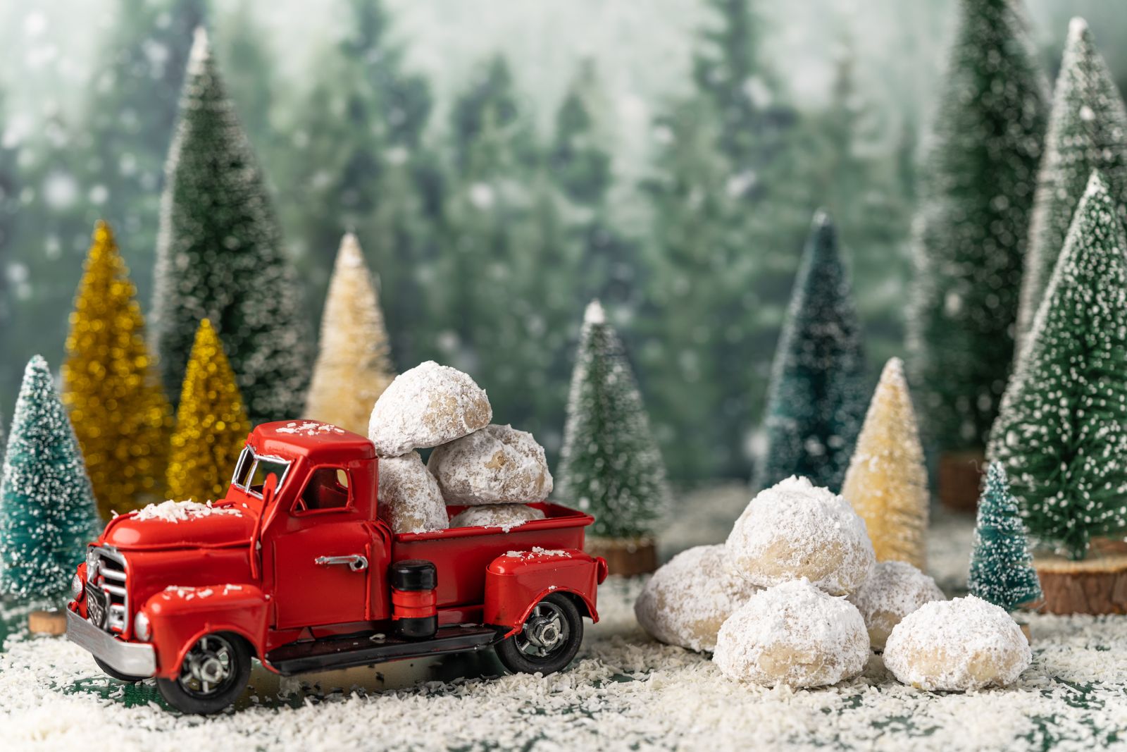 Powdered sugar snowball cookies with a red toy truck and mini Christmas trees