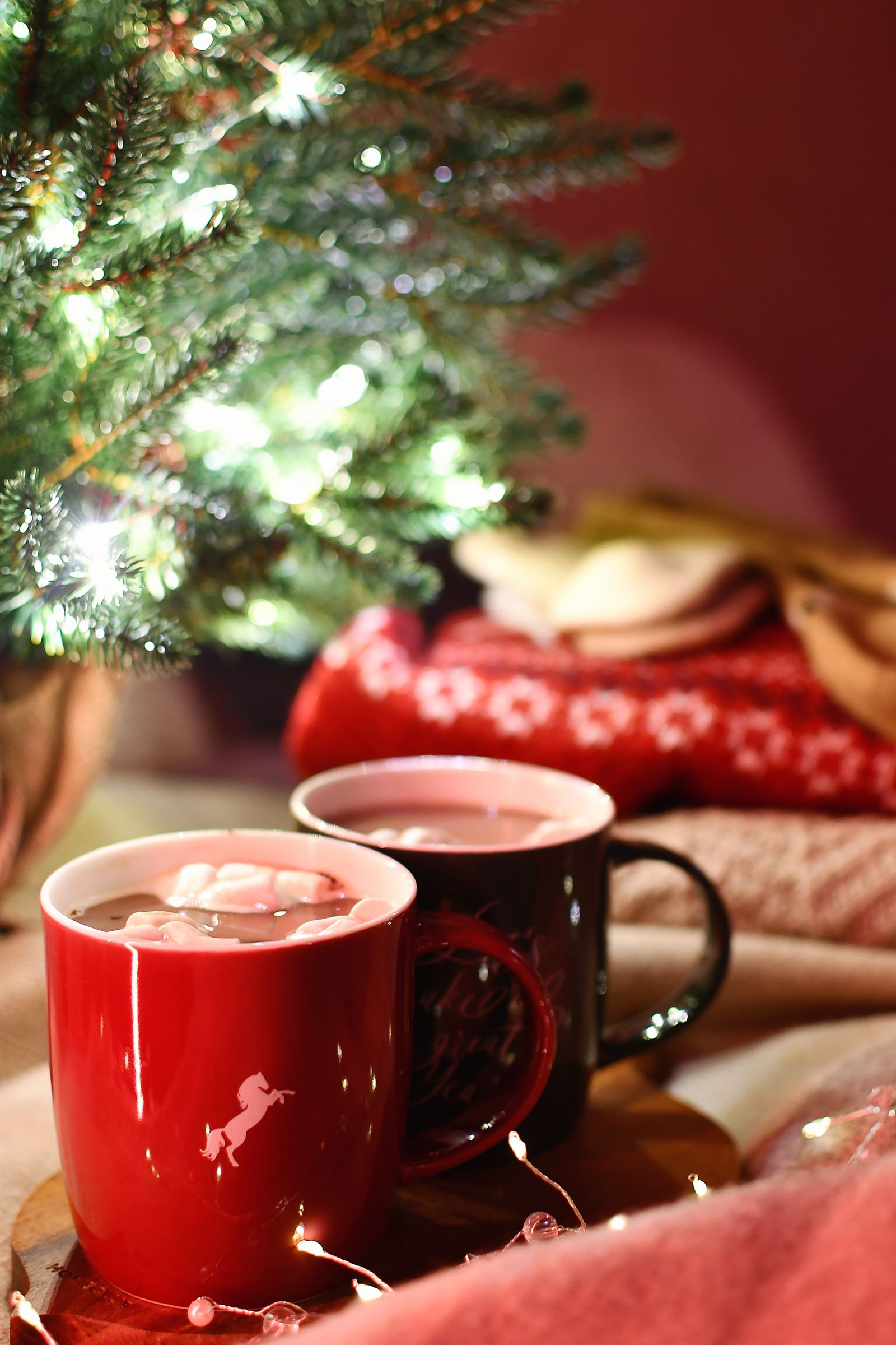 Two mugs of hot chocolate beside a lit Christmas tree
