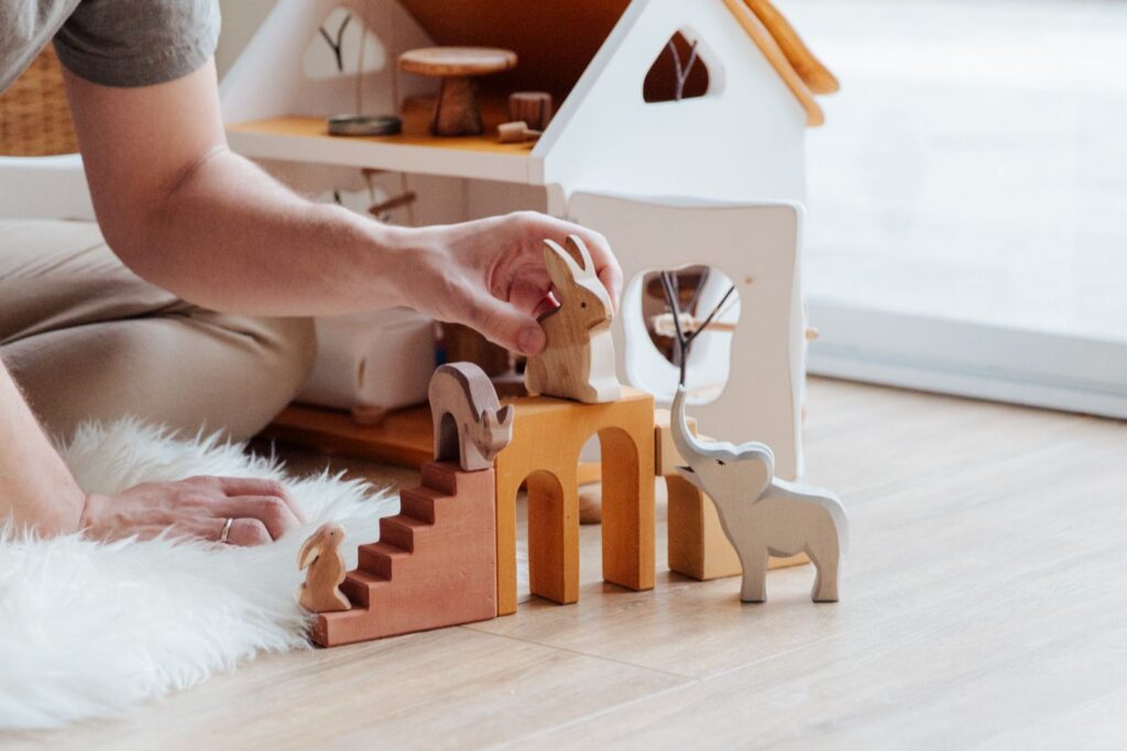 Hands setting up wooden animal toys on a playroom floor
